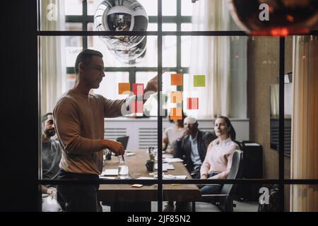 Mature businessman discussing over adhesive notes with colleagues in meeting room Stock Photo