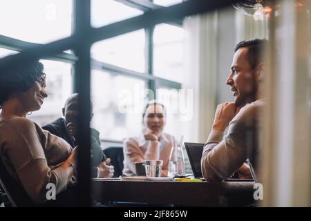 Mature businessman discussing plans with male and female colleagues sitting at conference table Stock Photo