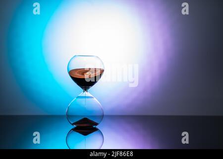 Hourglass standing on mirror surface in neon light Stock Photo