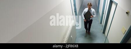 Young Man Stealing Computer Monitor Walking In Building Corridor Stock Photo