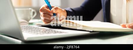 Close-up Of A Businesswoman's Hand Writing Note With Pen In Diary Over Desk Stock Photo