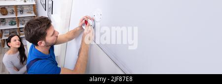 Happy Woman Standing Near Serviceman Replacing Battery In Smoke Alarm Stock Photo