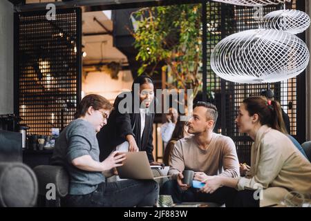 Young businesswoman discussing over laptop with male and female colleagues while sharing ideas in office Stock Photo