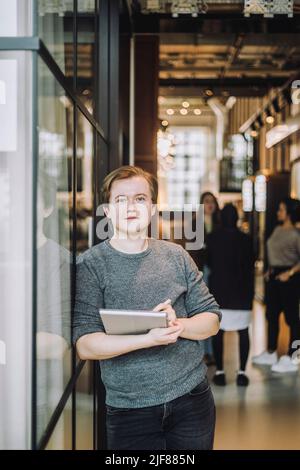Portrait of young businessman with laptop leaning on wall in creative office Stock Photo