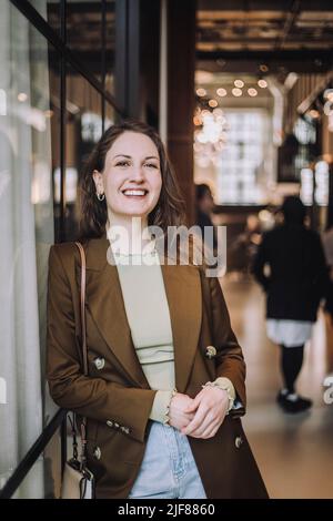 Portrait of happy mid adult businesswoman leaning on wall while standing in creative office Stock Photo