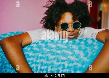Young hipster woman with sunglasses lying on blue blanket at home Stock Photo