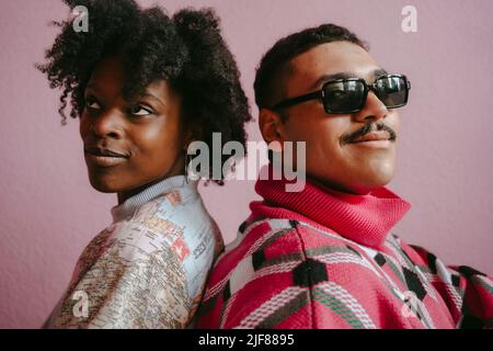 Thoughtful hipster woman with gay man against pink wall at home Stock Photo