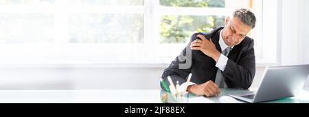 Mature Businessman Suffering From Shoulder Pain At Workplace Stock Photo