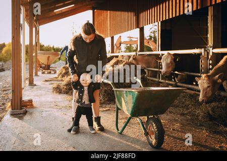 Mother holding hands of son while standing in stable Stock Photo