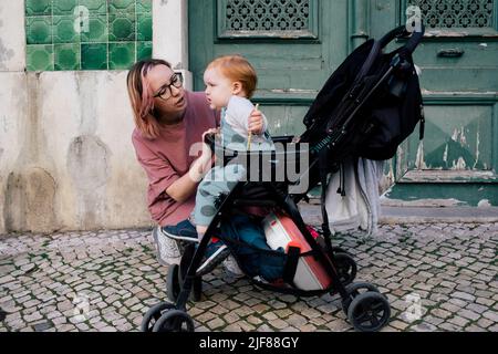 Mother looking at crying son sitting in baby stroller on footpath Stock Photo