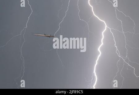 30 June 2022, Hessen, Frankfurt/Main: A flash flashes through the evening sky while an airplane (l) is approaching Frankfurt Airport. At an exposure time of 1/8 second, the aircraft is illuminated by the flash. Photo: Frank Rumpenhorst/dpa Stock Photo