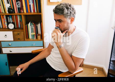 Contemplative depressed man sitting on chair in therapy office Stock Photo