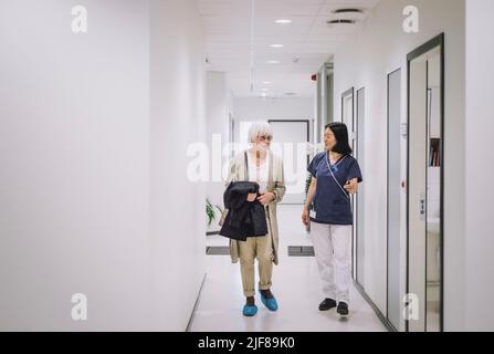 Full length of senior woman talking with female doctor while walking in corridor at medical clinic Stock Photo