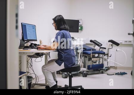 Side view of female doctor using desktop PC sitting at desk in medical clinic Stock Photo