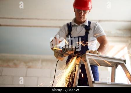 Professional construction worker hands in work gloves using angle grinder to cut metal rod at building site. Close up shot of contractor cutting iron Stock Photo
