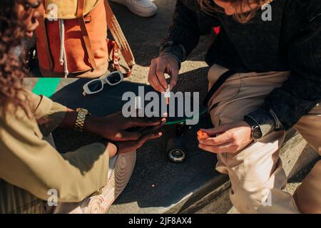 Midsection of man painting fingernails of female friend sitting near skateboard Stock Photo
