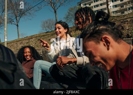 Happy woman gesturing while talking with multiracial friends on sunny day Stock Photo