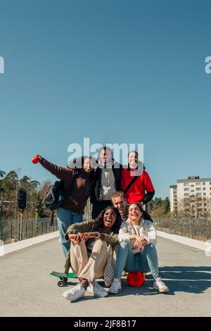 Happy multiracial friends having fun at railroad station platform against clear blue sky on sunny day Stock Photo