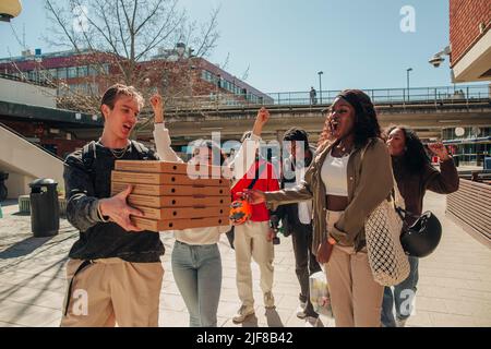 Man carrying stack of pizza boxes while walking with friends at street on sunny day Stock Photo