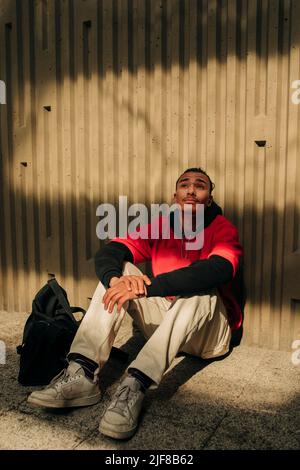 Thoughtful young man sitting against wall Stock Photo