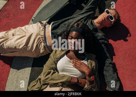 Young male and female friends lying down while relaxing in playground on sunny day Stock Photo