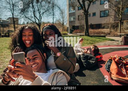Happy young friends sharing smart phone together in playground on sunny day Stock Photo