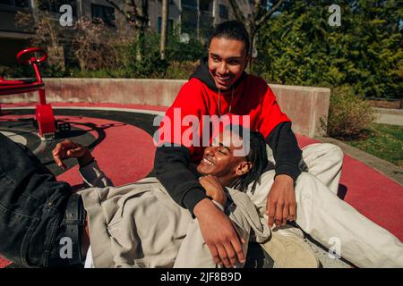 Cheerful young man lying on friend's lap in playground Stock Photo