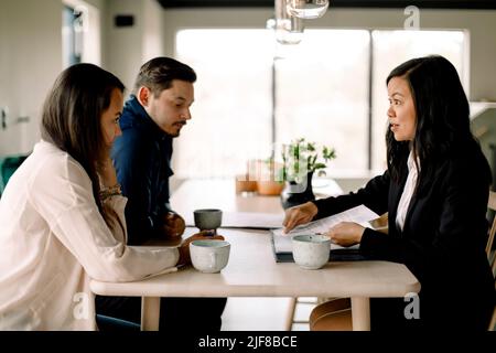 Customers discussing property documents with saleswoman at table in new house Stock Photo