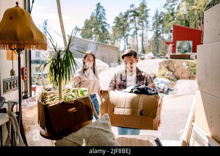 Couple picking cardboard boxes from delivery truck on sunny day Stock Photo