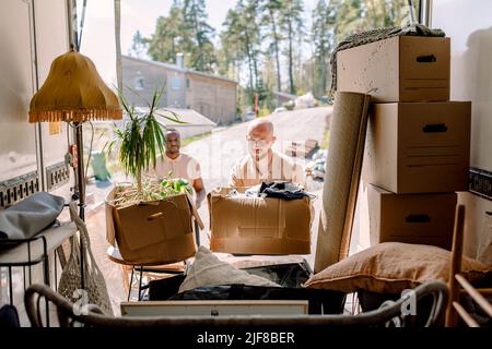 Multiracial movers unloading cardboard boxes from truck Stock Photo