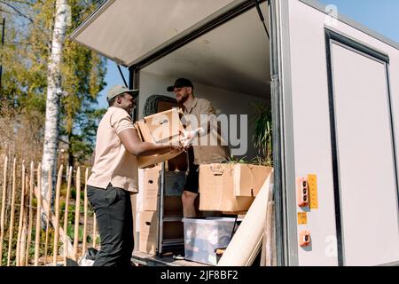 Multiracial movers unloading cardboard boxes from truck during sunny day Stock Photo