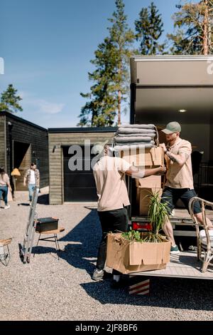 Delivery men picking cardboard boxes from truck during sunny day Stock Photo