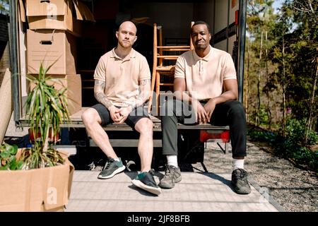 Portrait of multiracial movers sitting at trunk of delivery truck Stock Photo