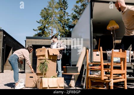 Couple opening cardboard boxes while delivery man unloading furniture from truck Stock Photo