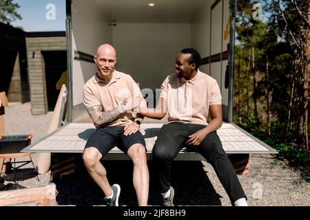 Smiling multiracial delivery men shaking hands while sitting in truck during sunny day Stock Photo