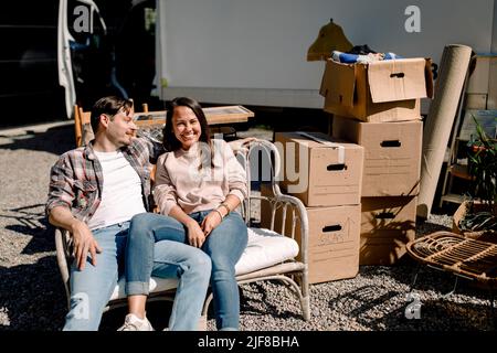 Smiling couple sitting on chair while relocating to new house Stock Photo
