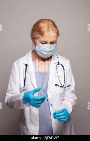 Doctor or nurse holding a syringe with liquid vaccines preparing to do an injection. Physician in white uniform, robe. Stock Photo