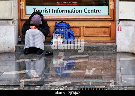 A homeless man shelters from the rain outside the Tourist Information Centre in Ljubljana, the capital of Slovenia. Stock Photo
