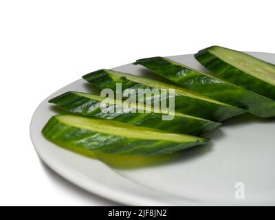 A smooth, medium-sized cucumber on a white plate. Cucumber on a yellow background. Sliced ​​vegetables. Vegetable isolate. Stock Photo