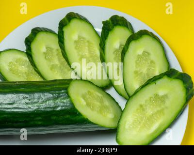 A smooth, medium-sized cucumber on a plate, sliced. Cucumber on a yellow background. Vegetable isolate. Stock Photo
