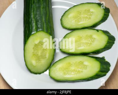 A smooth, medium-sized cucumber cut into slices. Cucumber on a plate. Vegetable isolate. Fresh ripe vegetable before cooking dinner. Stock Photo