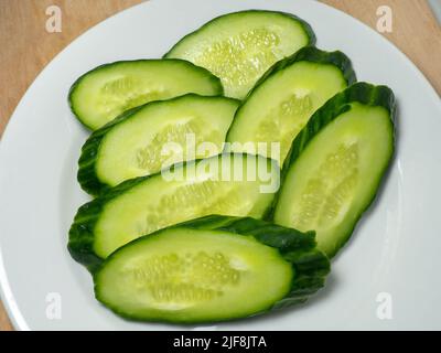 A smooth, medium-sized cucumber cut into slices. Cucumber on a plate. Vegetable isolate. Fresh ripe vegetable before cooking dinner. Stock Photo