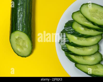 A smooth, medium-sized cucumber on a plate, sliced. Cucumber on a yellow background. Vegetable isolate. Stock Photo