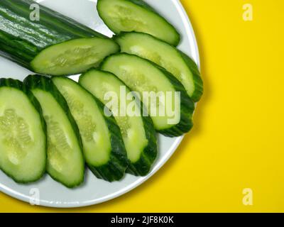 A smooth, medium-sized cucumber on a plate, sliced. Cucumber on a yellow background. Vegetable isolate. Stock Photo
