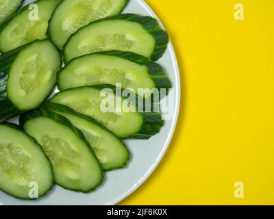 A smooth, medium-sized cucumber on white plate, sliced. Cucumber on a yellow background. Vegetable isolate. Stock Photo