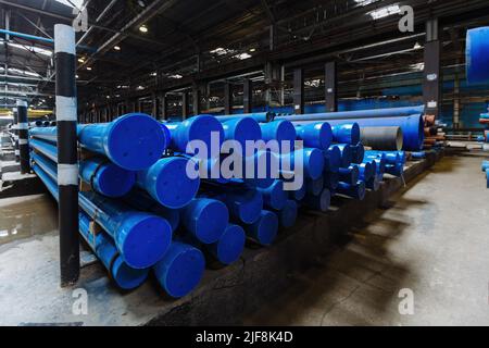 New blue colored cast iron pipes with caps for pipeline construction in warehouse. Stock Photo