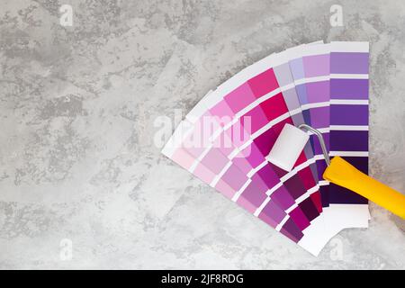 Colour Palette Catalog purple samples and roller for wall painting , paint selection cards on grey stone background Stock Photo