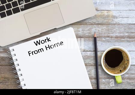 Work From Home written on a blank notepad with laptop computer,pencil and cup of coffee on wood table with copy space. Stock Photo