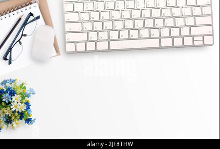 White minimal office desk table with notebook,glasses and flower and mini mouse and keyboard wireless. Top view with copy space for text or picture, f Stock Photo