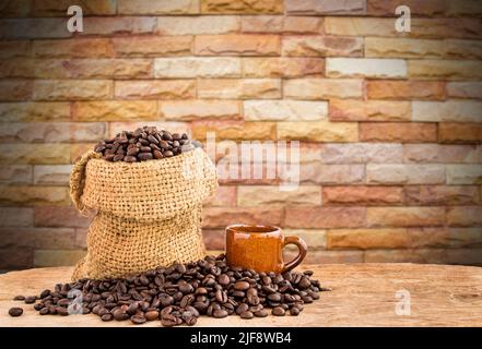 Coffee beans in burlap sack on wooden table with blurred brick wall background Stock Photo